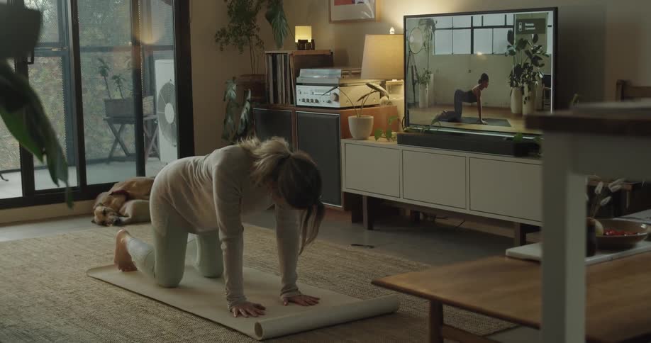 A woman follows a woman on television doing yoga