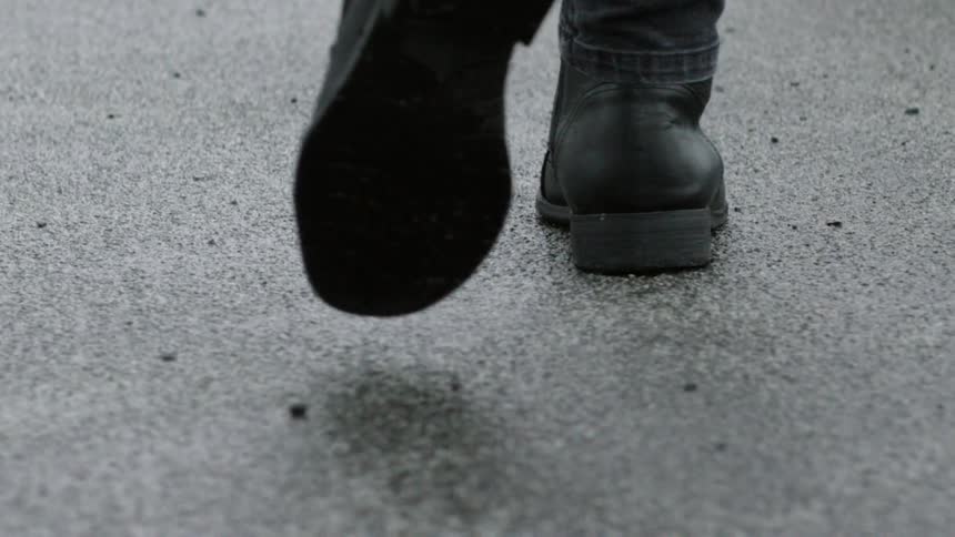 A person wearing boots and jeans walks on a wet street