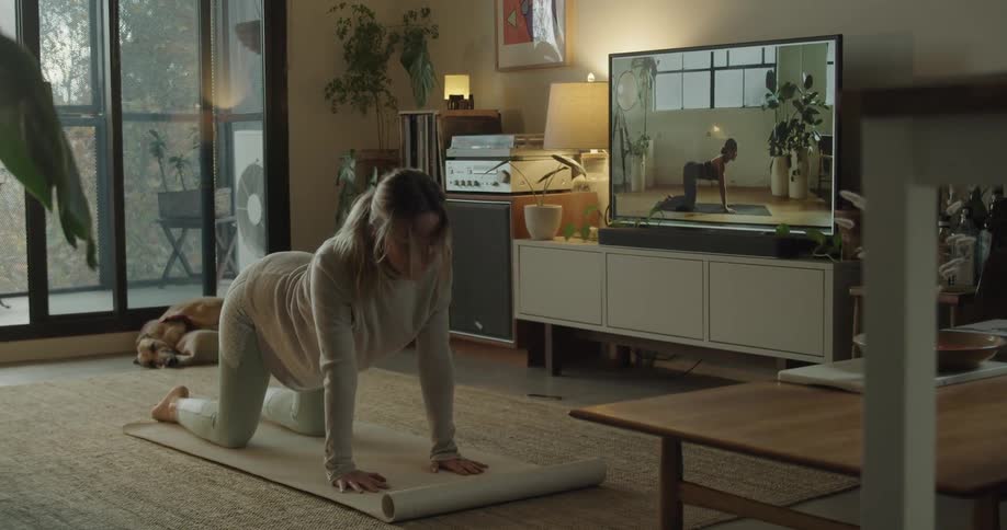 A woman practicing yoga while watching an yoga instructional video on television