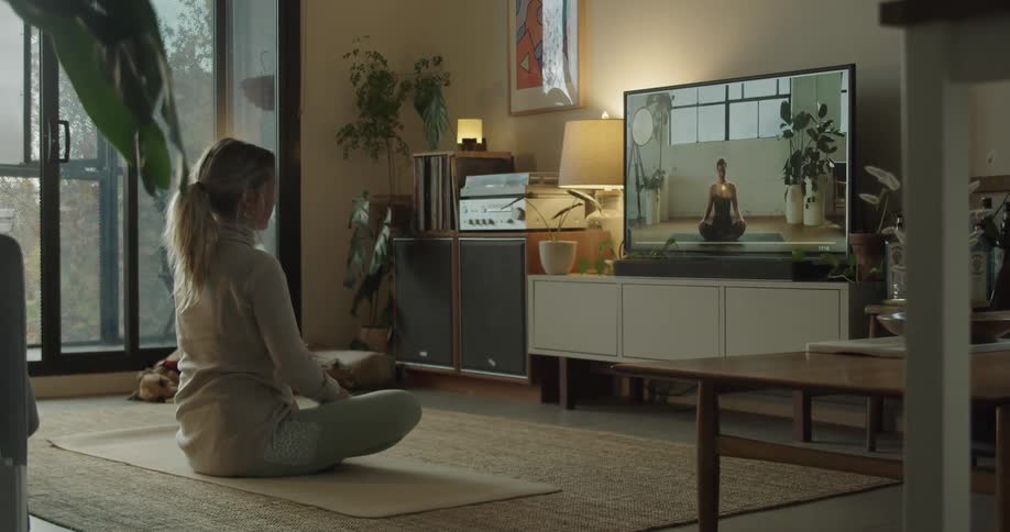 Woman sitting in living room floor follows yoga class on television