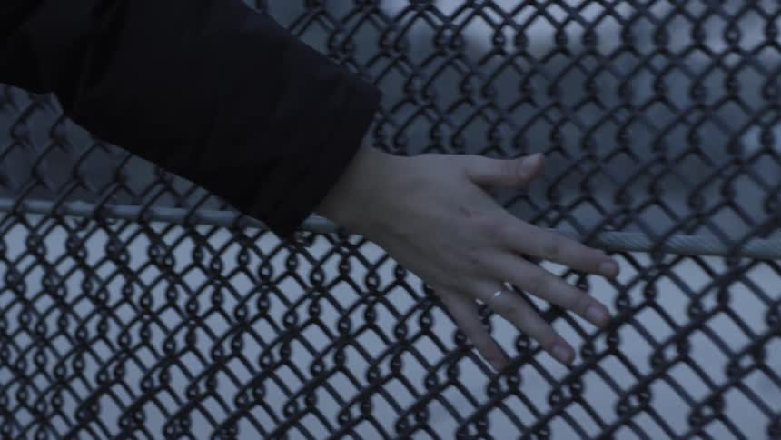 Person wearing ring runs hand along chain link fence