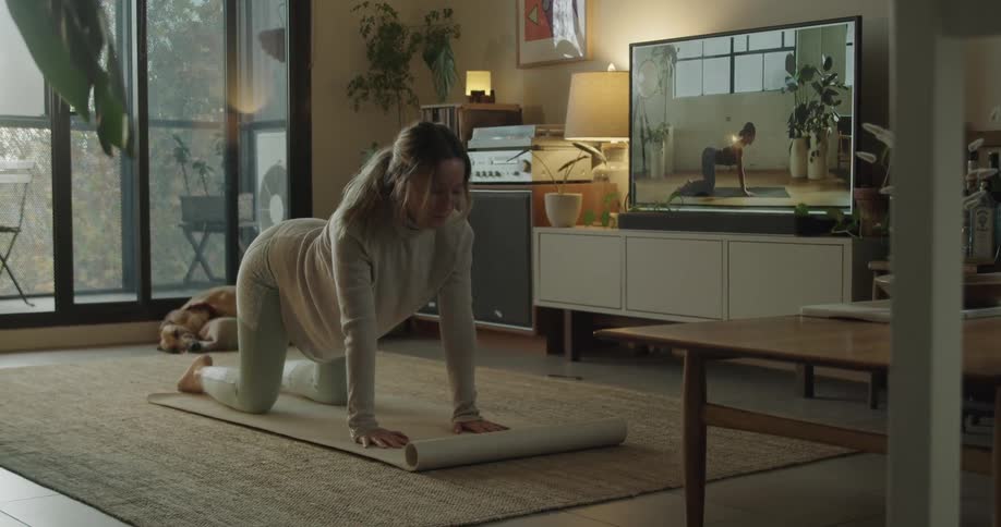 A woman does yoga while following an instructor on television