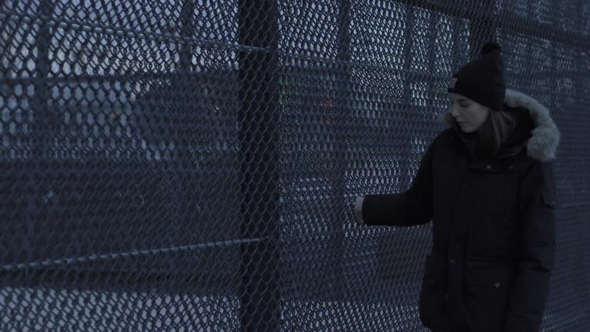 A woman runs her hand along a fence as she walks past it