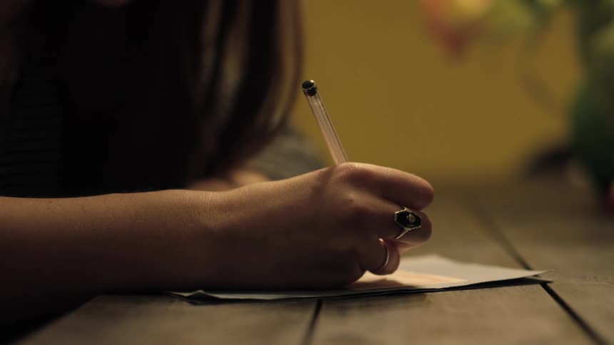 A white woman sits at a table and rights on a piece of paper