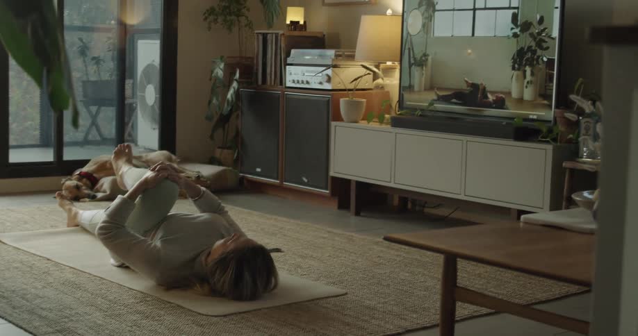 A white woman exercises with yoga on a rug in a living room
