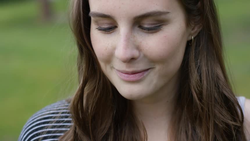 A woman smiles as she smells some pink flowers