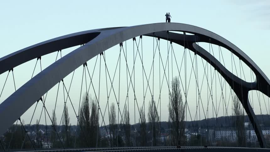 Two people climb over a bridge structure and hug on top