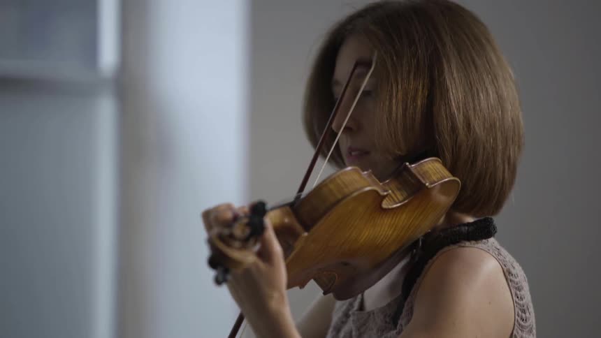 Woman stands alone in a room playing the violin