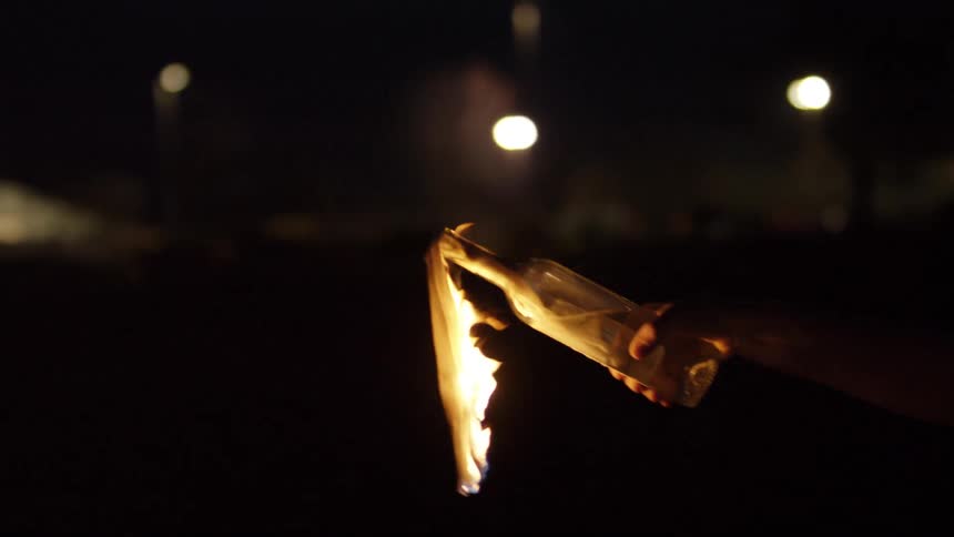 A man at night lighting a molotov cocktail