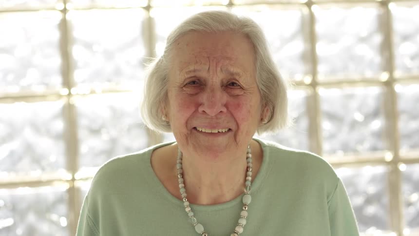 An elderly white woman smiles and blinks