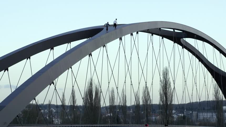 Two people run parkour style over the arch of a bridge