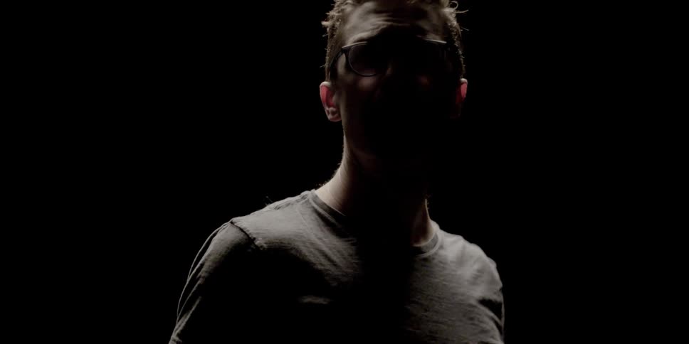A man standing in the darkness turns towards the camera