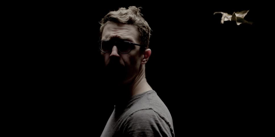 Man looks back over his shoulder while a dry leaf falls down in the pitch black room