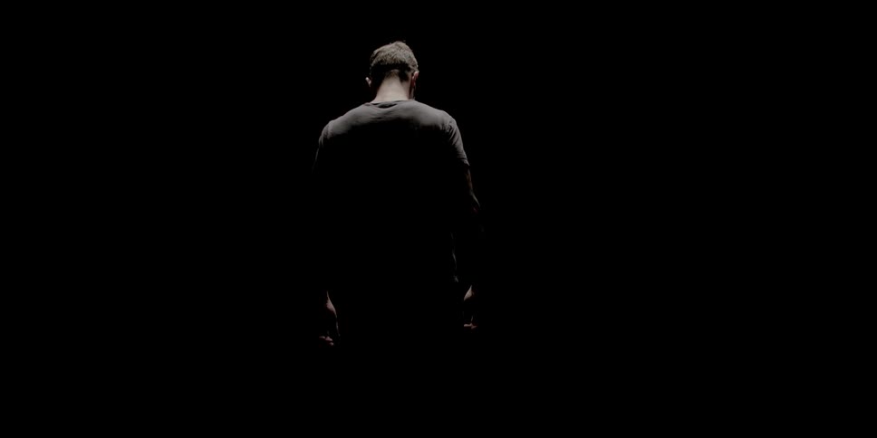 A man walks away with head hanging in a dark room