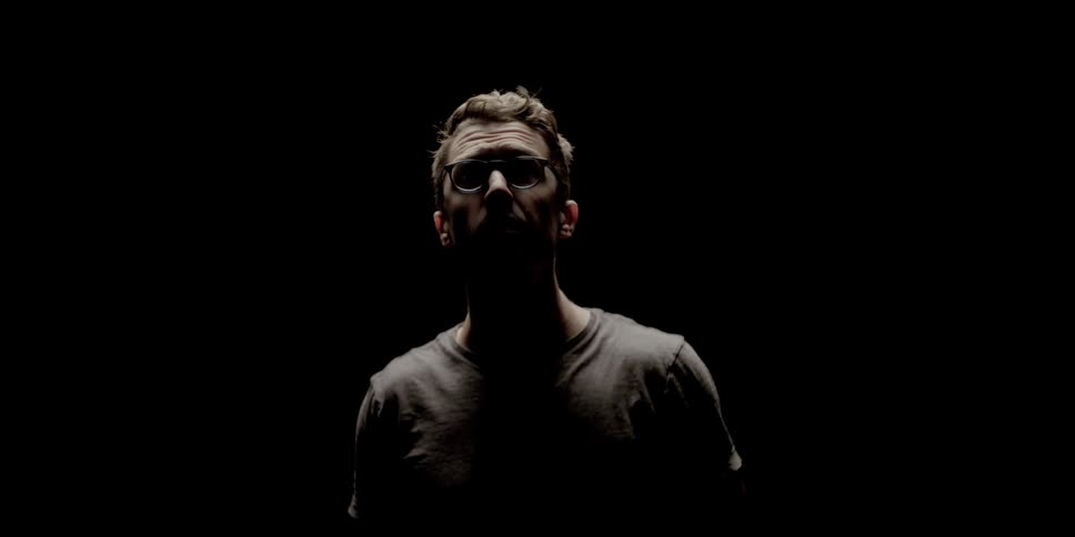A man wearing glasses looks up towards a light