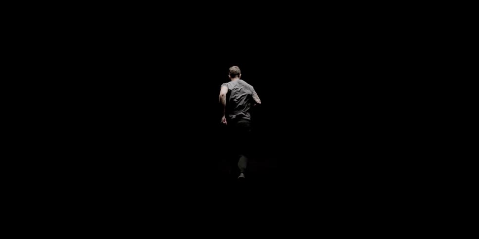 Man running in dark room passes under a single light