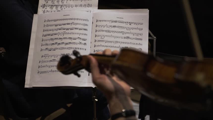 A person is playing a violin in front of sheet music