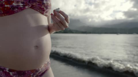 A pregnant woman in a swimsuit standing on a beach
