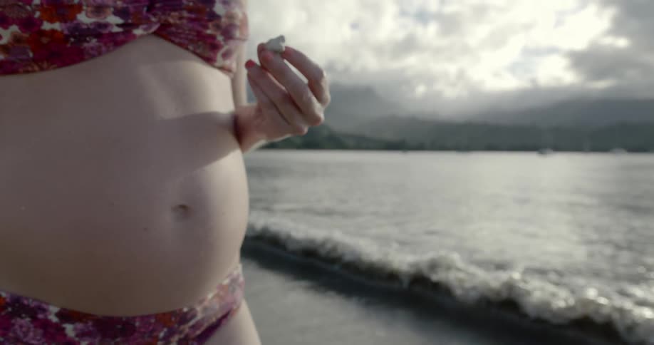 A pregnant woman in a swimsuit standing on a beach