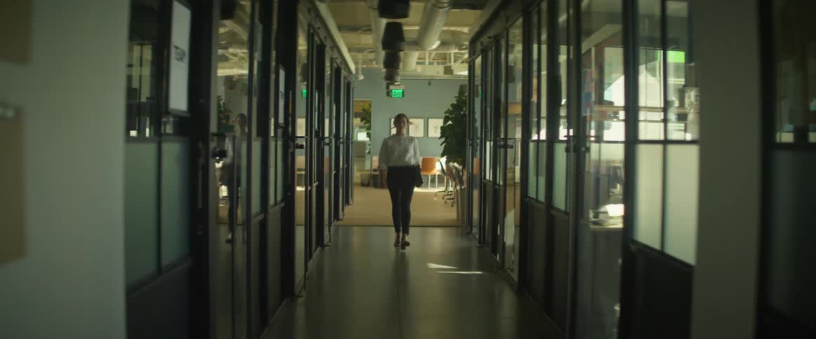 A woman walks down an office hallway holding something in her hand
