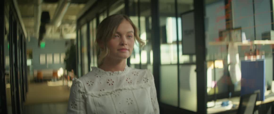 A woman in a lace blouse confidently walks through an office hallway