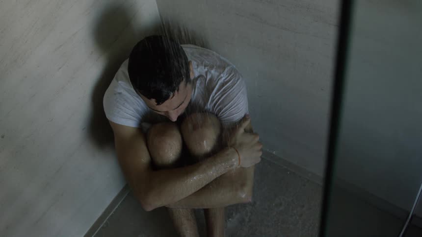 A man sits on the shower floor with the water running in his clothes