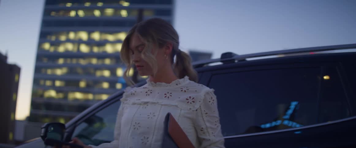A woman gets out of her car and uses her phone as she walks