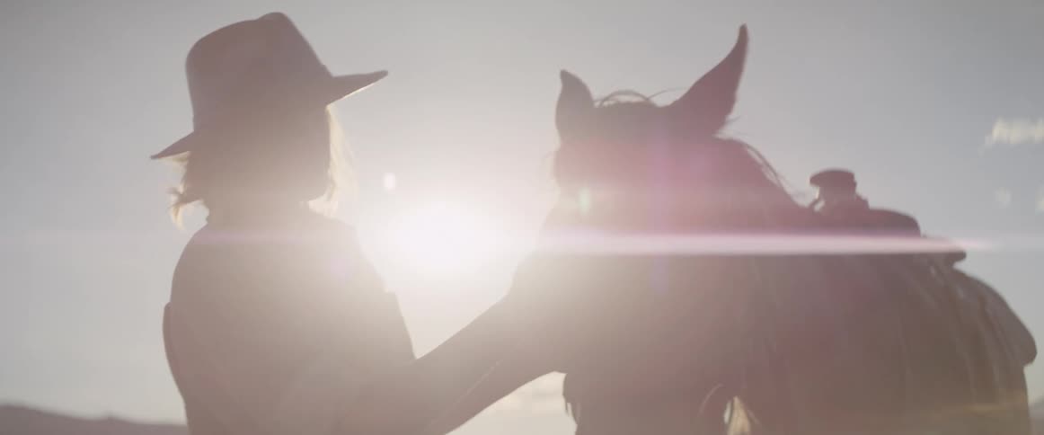 A woman with a hat standing and petting a horse