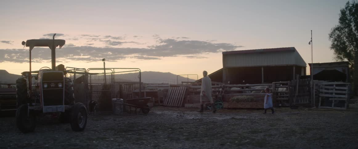 A small child following a farmer as they walk across a farm