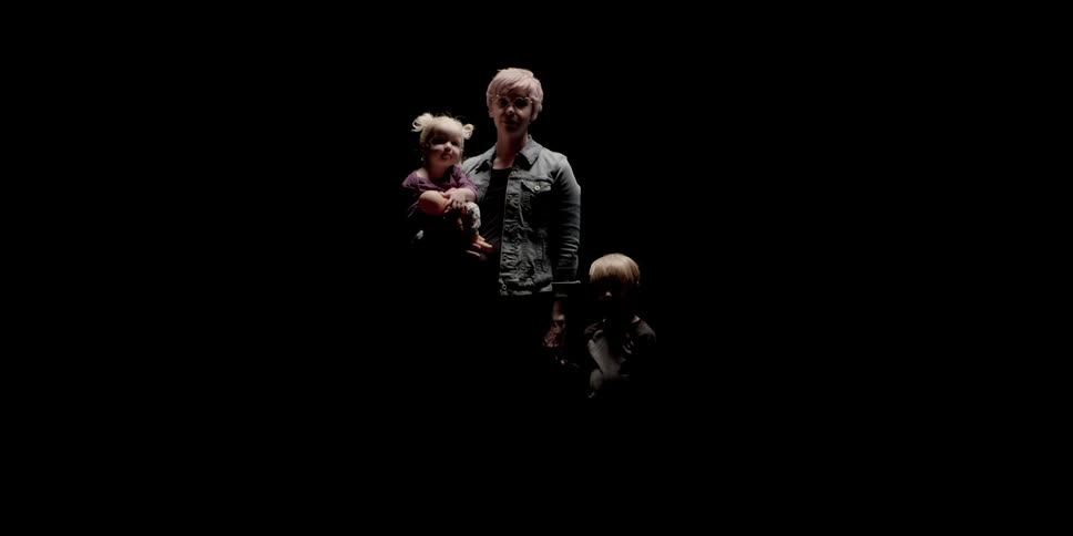 A mother with two children stands in a black room
