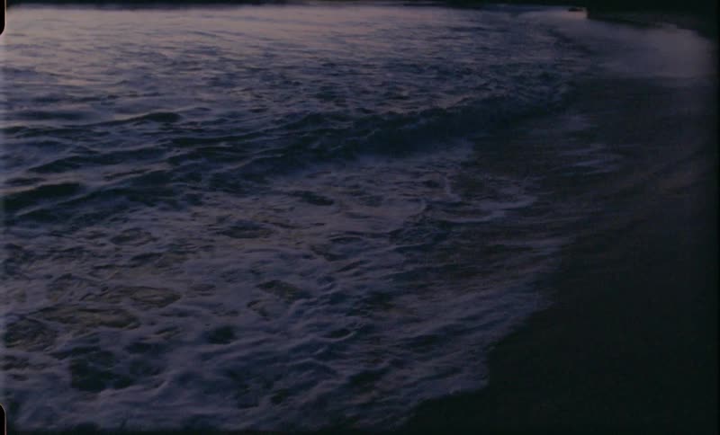 Sky near horizon glows orange as waves crash on the beach