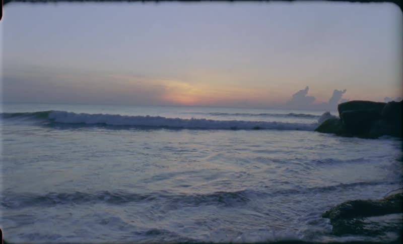 Waves crashing onto the shore of a boulder strewn beach during sunset