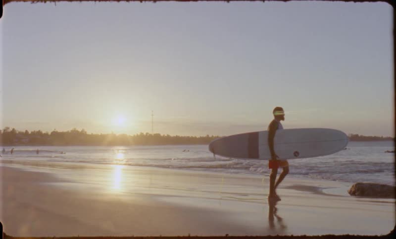 A man walks along the beach carrying a surf board