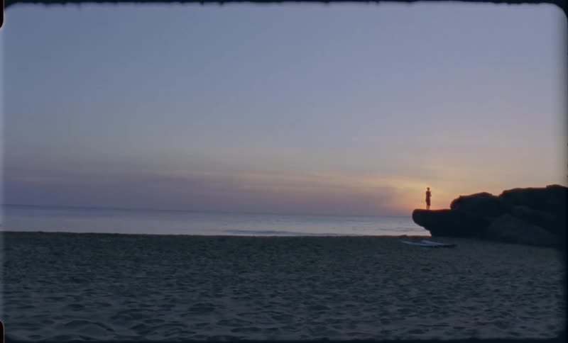 The silhouette of people on the rocks above the sandy beach at sunset