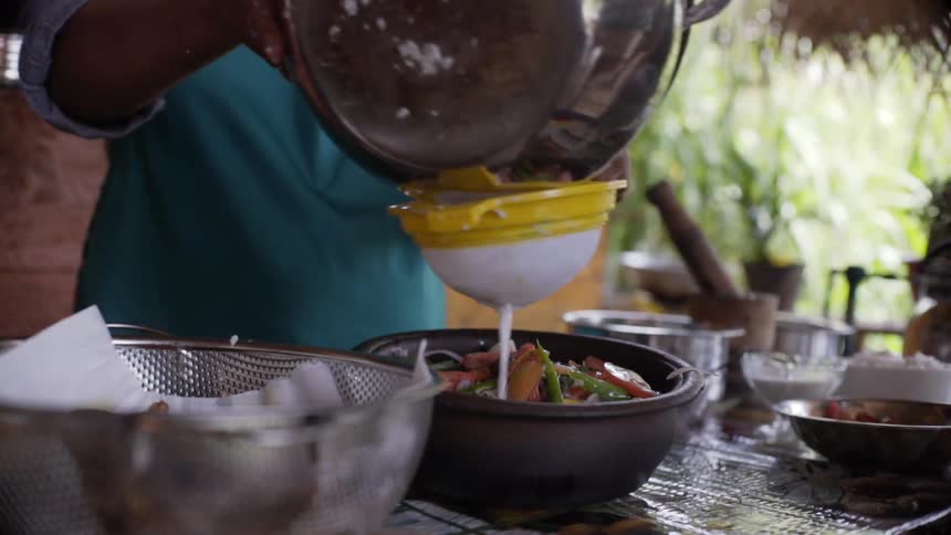 Person pours sauce over dish through sieve at counter