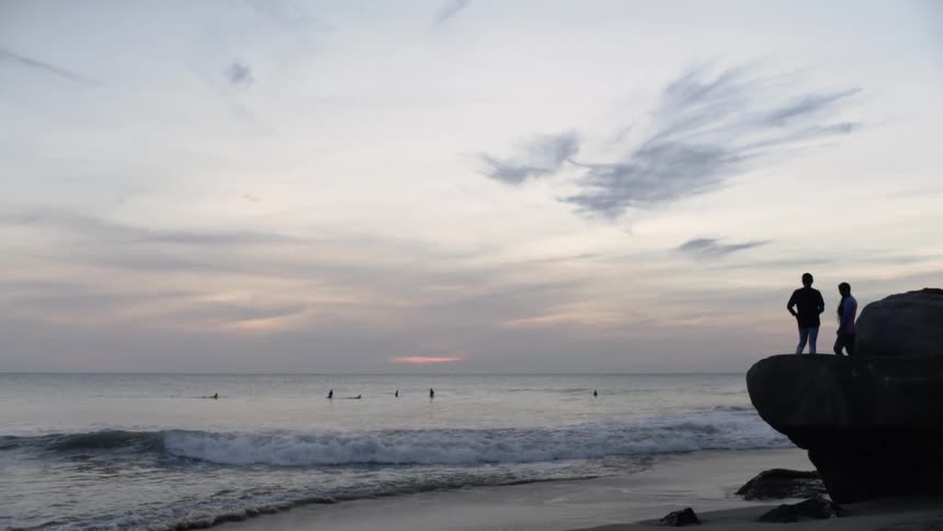 Silhouette of couple watching surfers from platform of a rock at sunrise