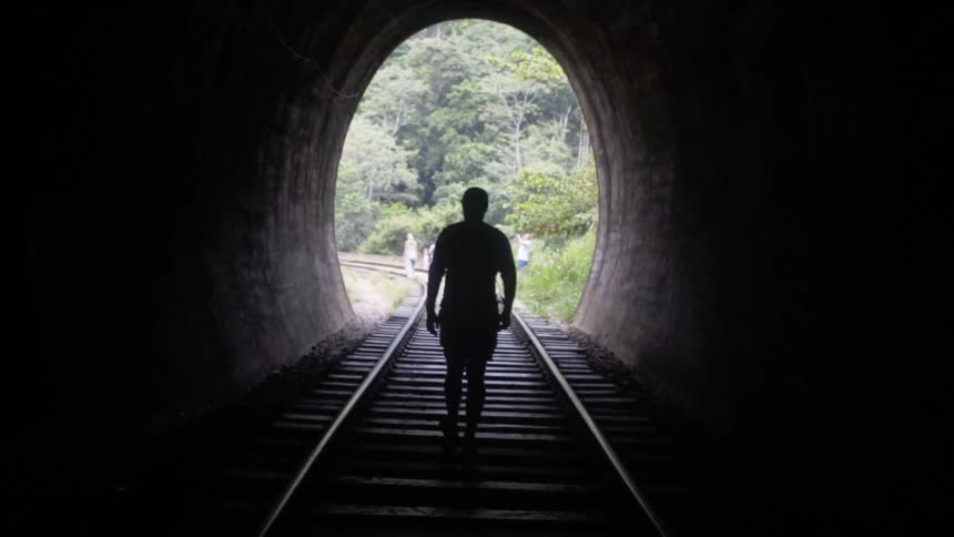 Silhouette of a man walks along the railroad through the tunnel