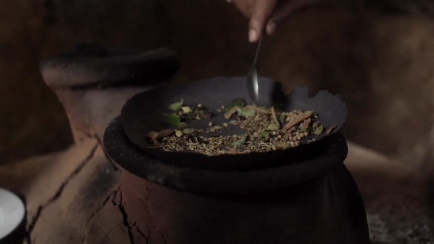 A person roast spices and herbs in a primitive stove