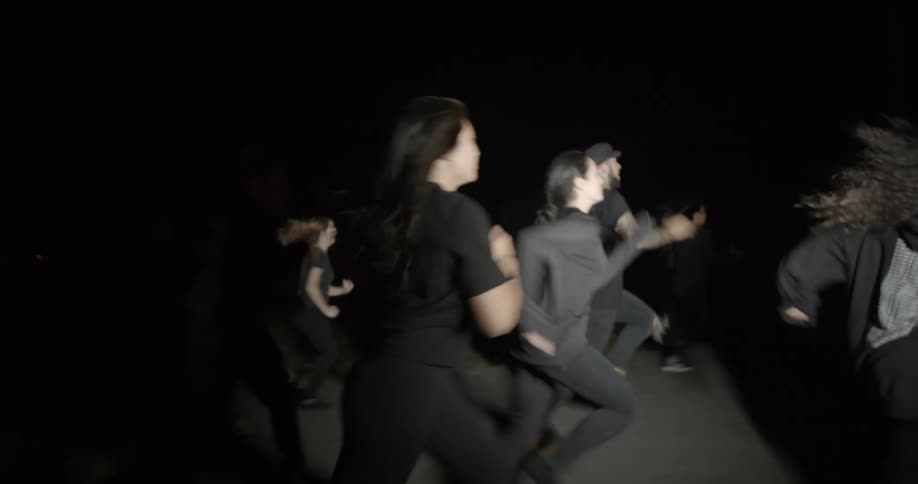 A group of people dressed in black run outside in the dark