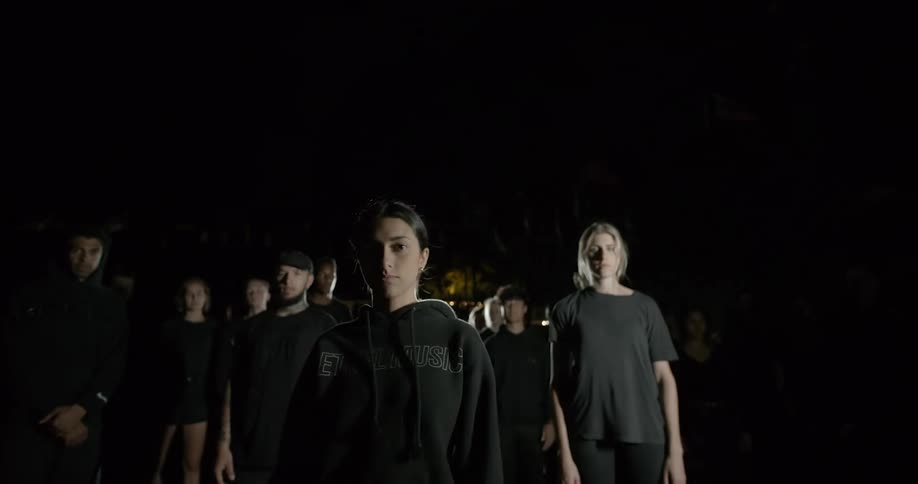 People wearing black standing in the dark with light shining on them
