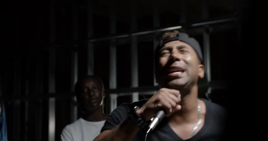 A black man raps indoors to a crowd of people