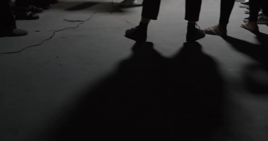 Peoples feet standing around next to a wire with their shadows moving back and forth