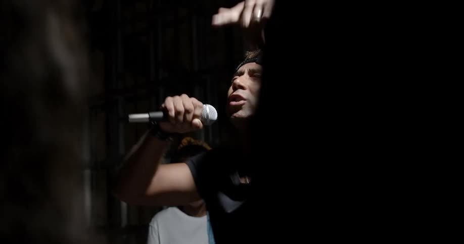 Black rapper rapping to a small female crowd gathered around him indoors