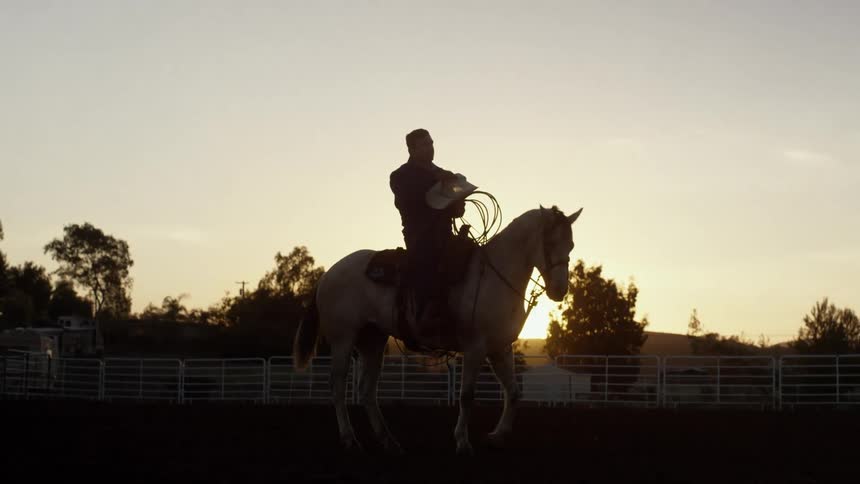 A cowboy on a horse in a fenced off field at sunrise
