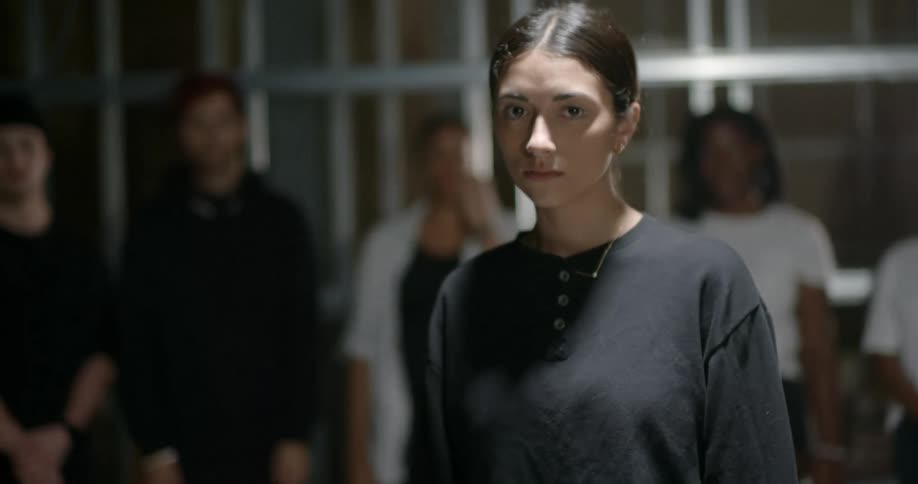 Woman walks forward from a group of people and looks at the camera