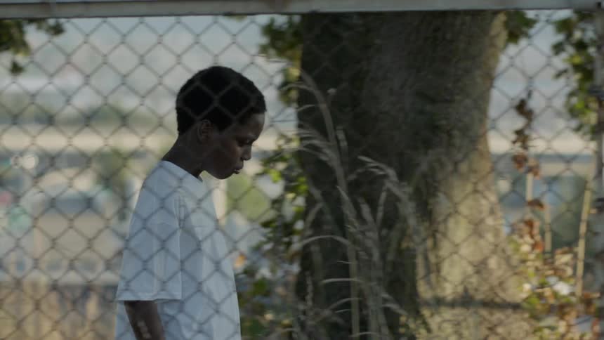 A young boy walks along a fence outside by himself
