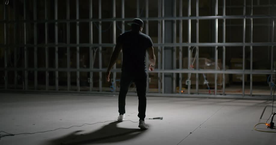A man walks into an empty framed room with a microphone on the floor and picks it up and poses