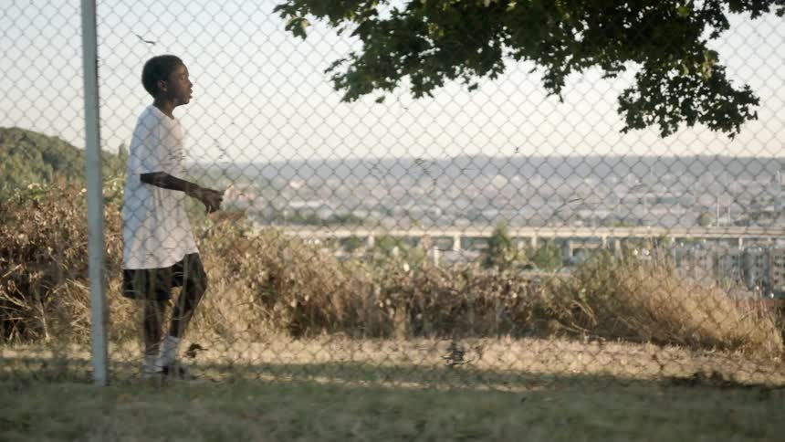 Black boy walks near the wire fence against the skyline