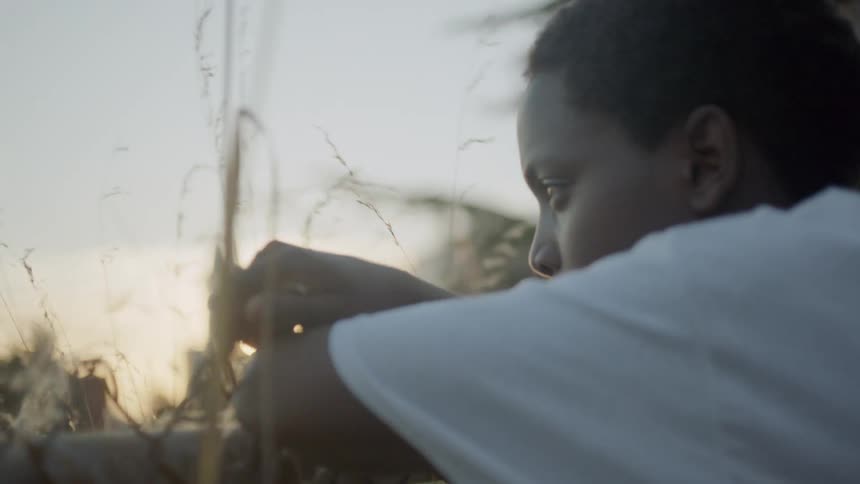 A boy leans against a chainlink fence at dusk
