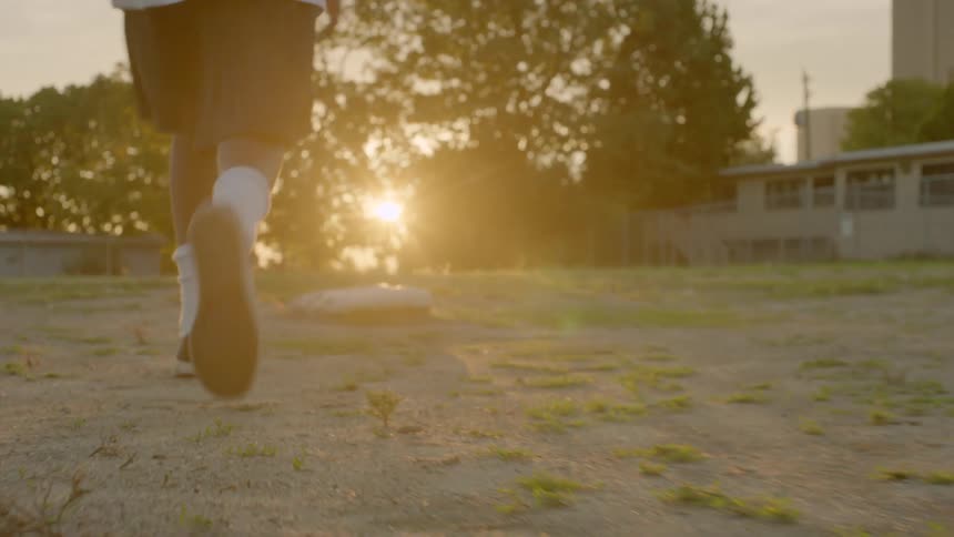 Kid walks over a baseball base in a field at sunset